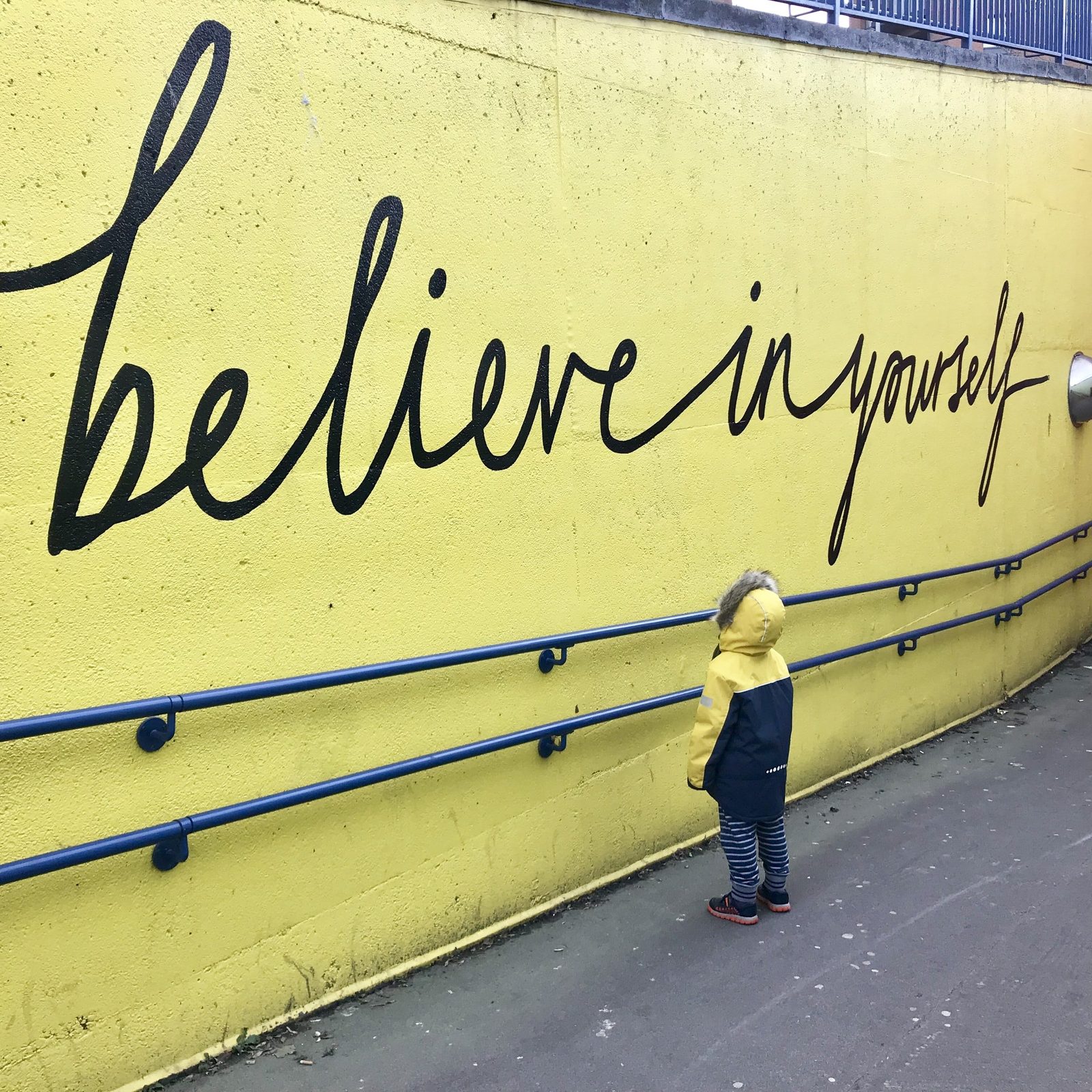 Graffiti reading “believe in yourself” on a yellow wall