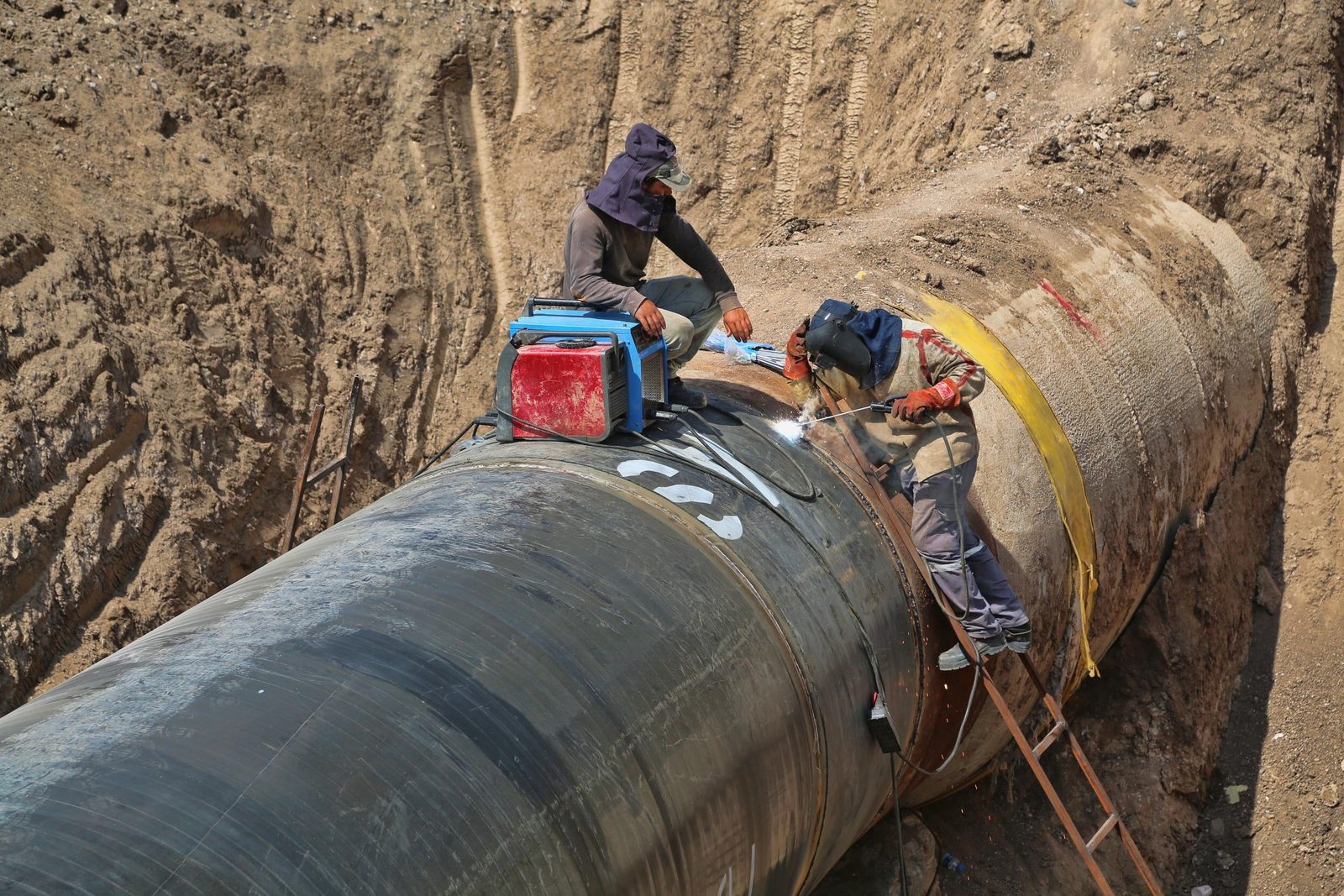 Workers joining a section of large pipeline in a trench